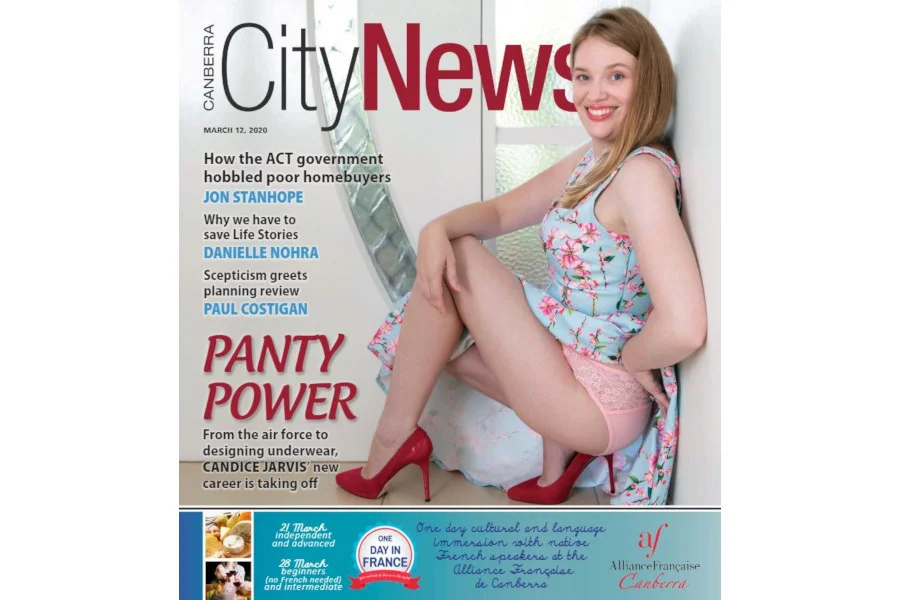 Founder of Candis Creations, wearing pink lace underwear and red high heels, seated against a white background on the cover of Canberra City News.