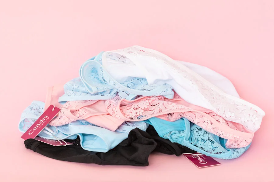 A collection of Candis lace underwear in assorted colors on a pink backdrop, embodying sustainable underwear recycling 2024.