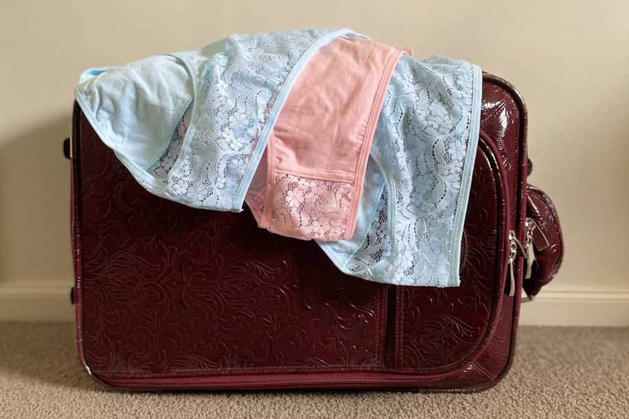 A burgundy suitcase with Candis lace underwear in pastel blue and pink spilling out, indicating travel readiness.